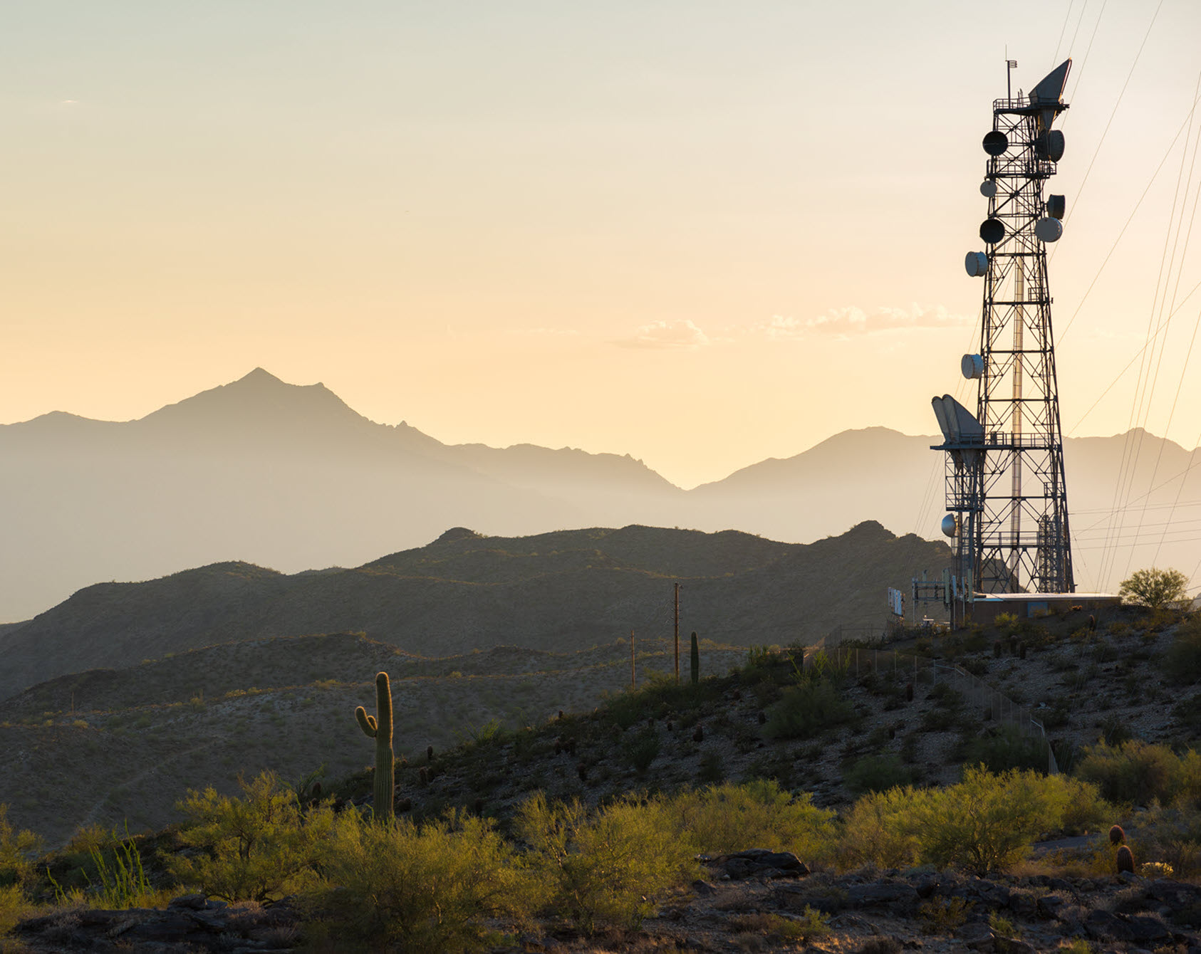 Landscape image of an industrial cell tower in the middle of a desert mountain range.