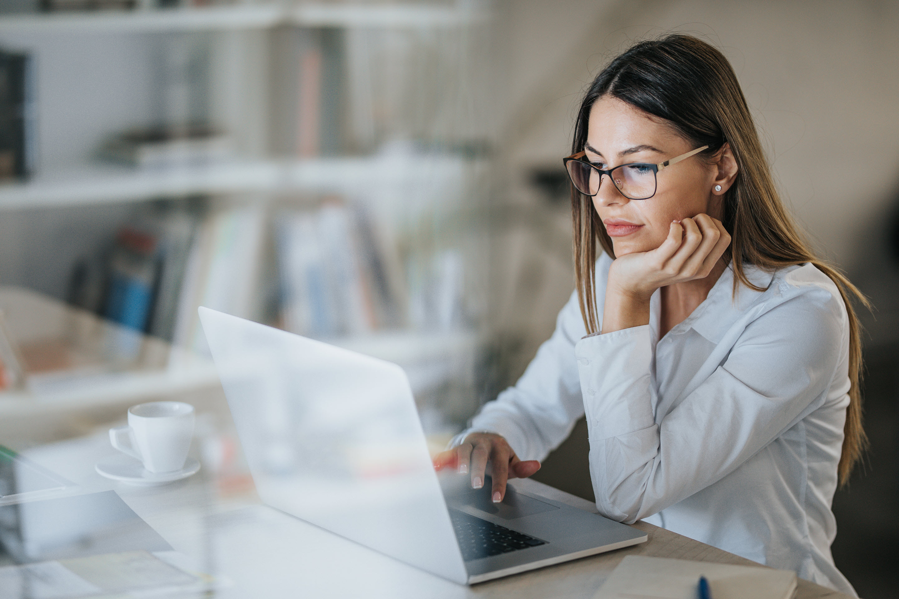 A young woman using her laptop, reading something on the screen thoughtfully.