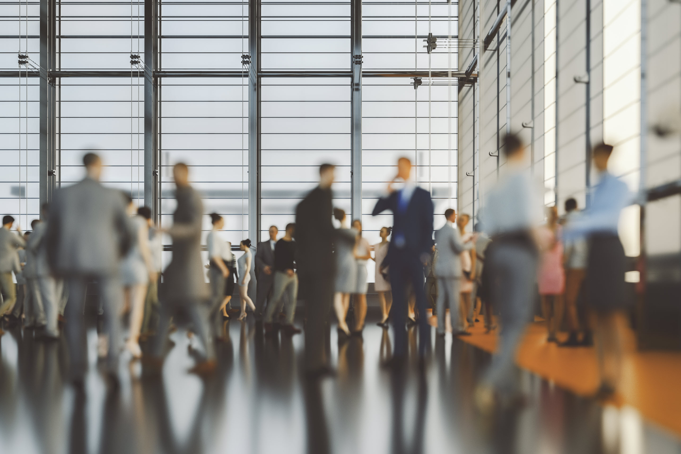 A conference room with large floor-to-ceiling windows, allowing natural light in. A crowd of businesspeople in formal clothing takes up most of the image, with many of the people interacting with one another: holding conversation, shaking hands, et cetera. The people are all blurred, as if they are in motion.