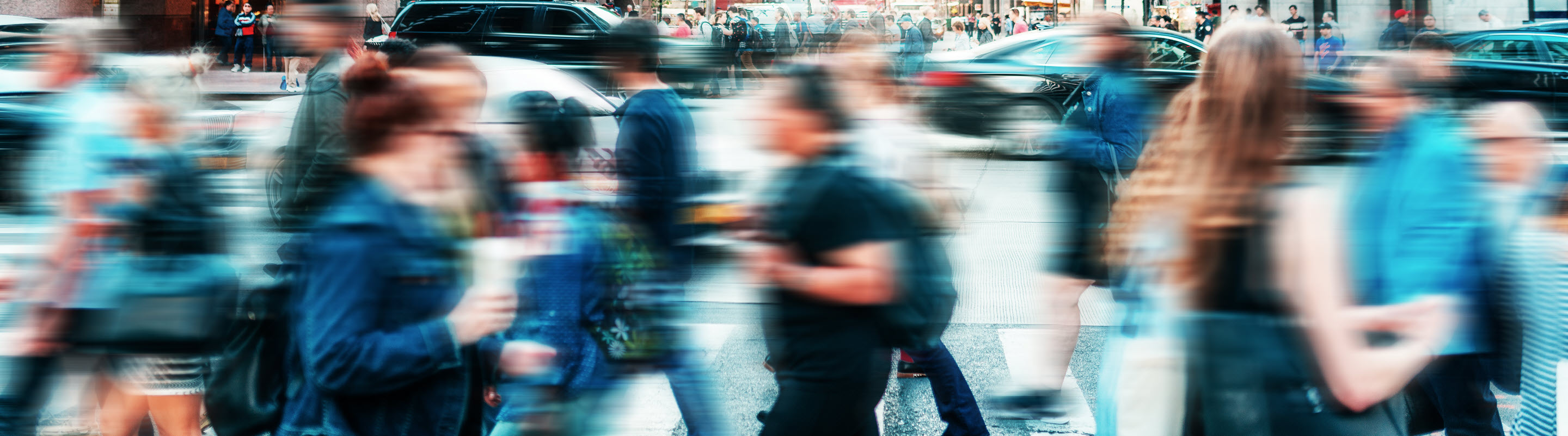 A busy city street, filled with a blur of people crossing at the crosswalk.