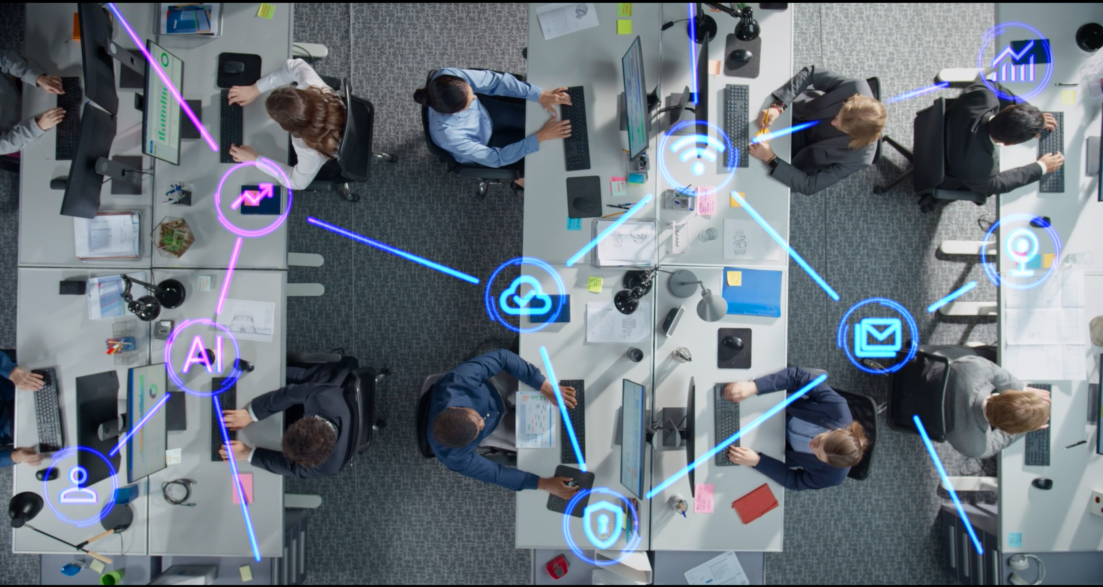 An overhead image of people working in an office. A graphic is overlayed on the image - it looks like a connected web that utilizes different technology icons (like email, AI, etc) at the web's connection points.