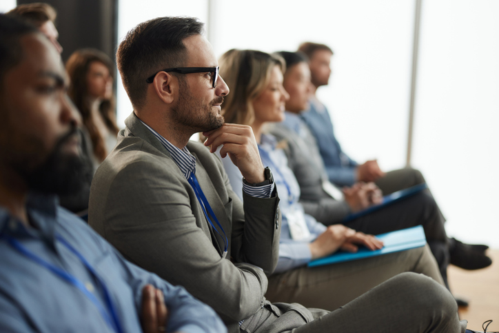 A group of business professionals look on, sitting in a user group.