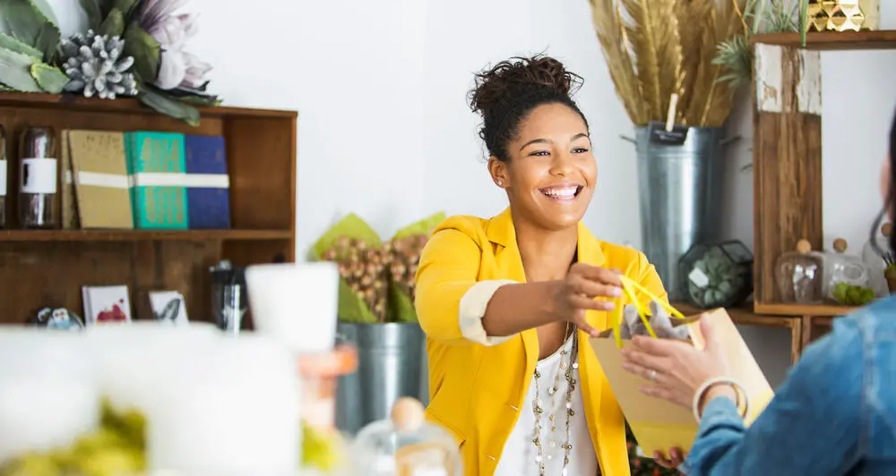 A smiling shop owner handing someone their purchase