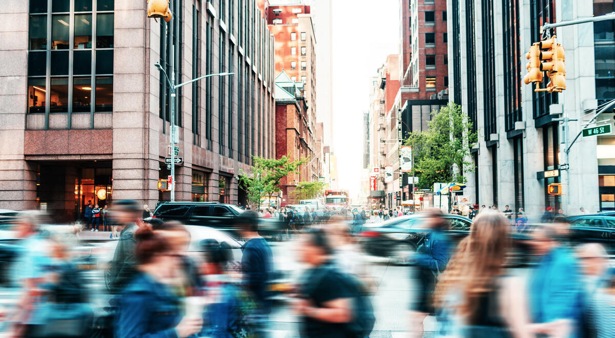 A busy city street, filled with a blur of people crossing at the crosswalk.