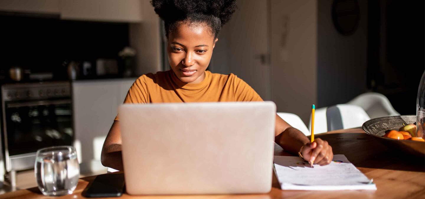 Young woman reading from the computer and taking notes at her notebook