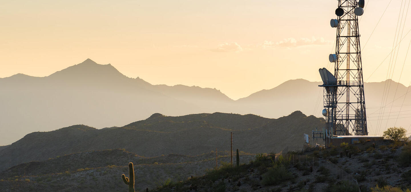 Landscape image of an industrial cell tower in the middle of a desert mountain range.