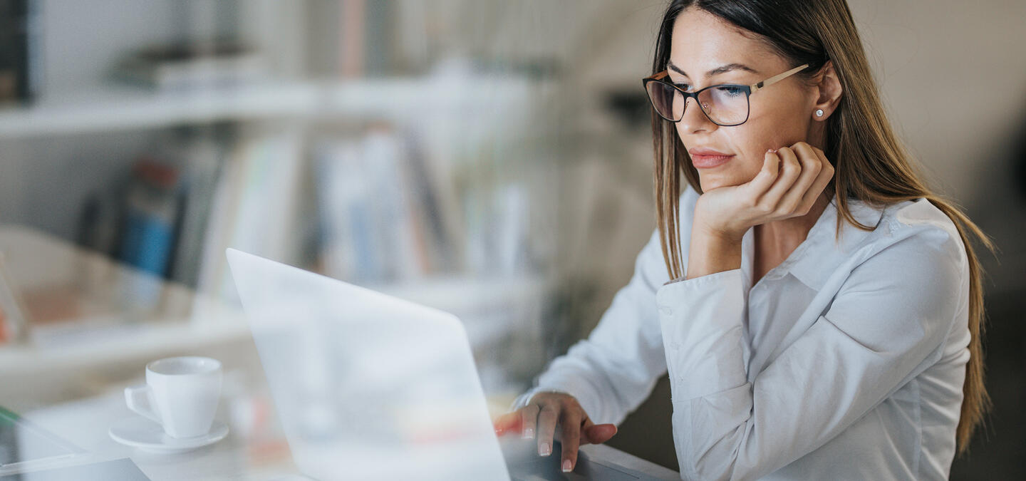 A young woman using her laptop, reading something on the screen thoughtfully.