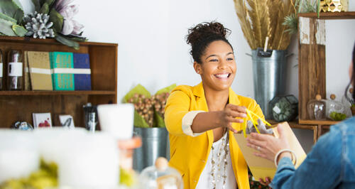A smiling shop owner handing someone their purchase