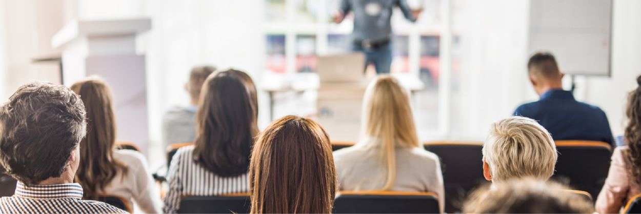 A seated group of customers listen to a presentation given by a subject matter expert.