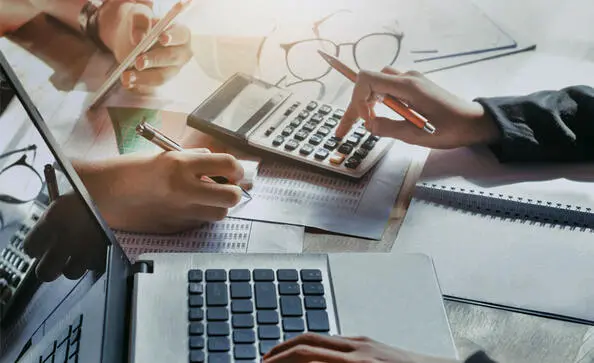 Two individuals working together using a laptop and calculator to review tax numbers.