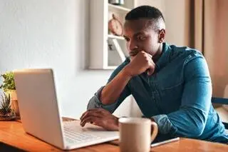 A man works from home, looking intently at his laptop.