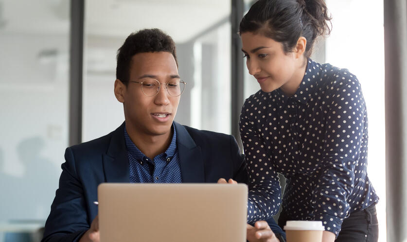 A tax technology professional assists another, using his laptop, in order to implement a seamless ERP upgrade.