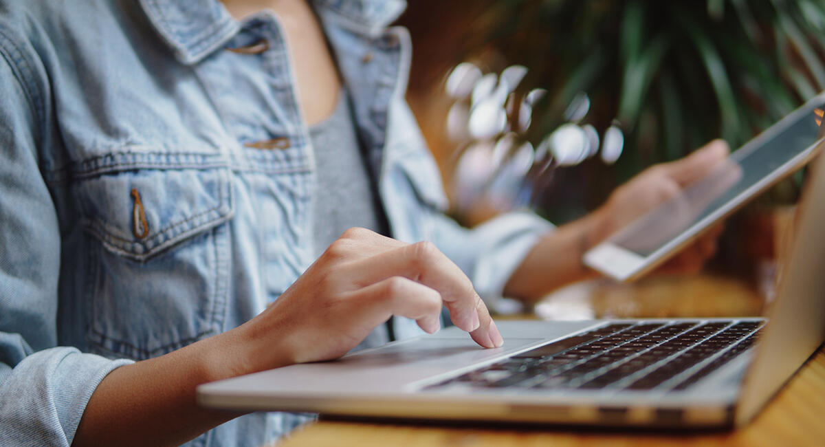 Person typing on laptop while holding a tablet.