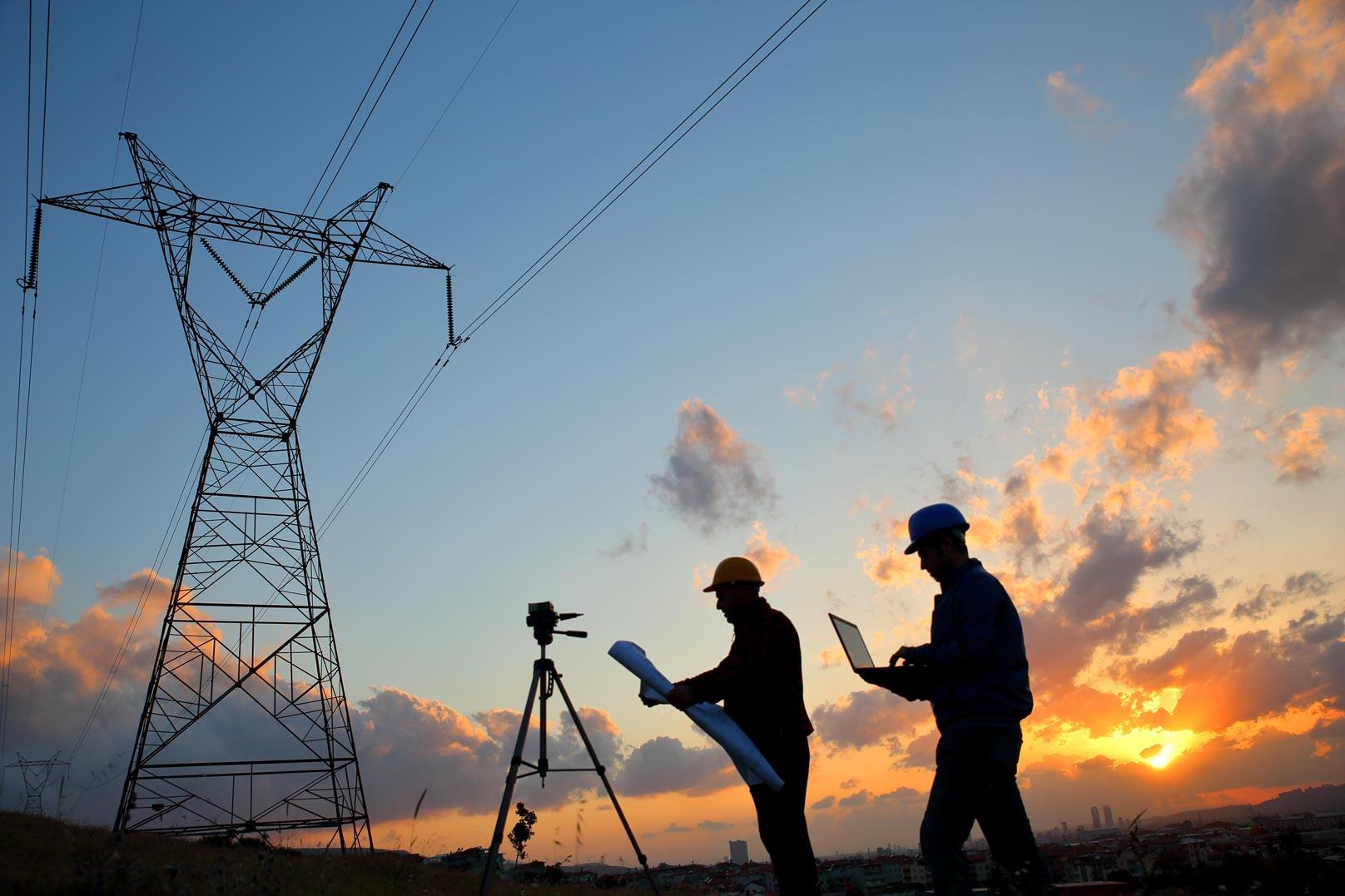 Workers stand near power lines with a bright sky behind them.