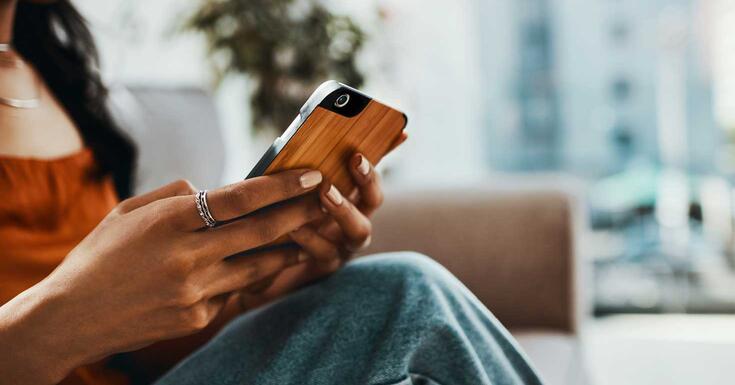 Cropped shot of a woman using a smartphone while relaxing on the sofa at home