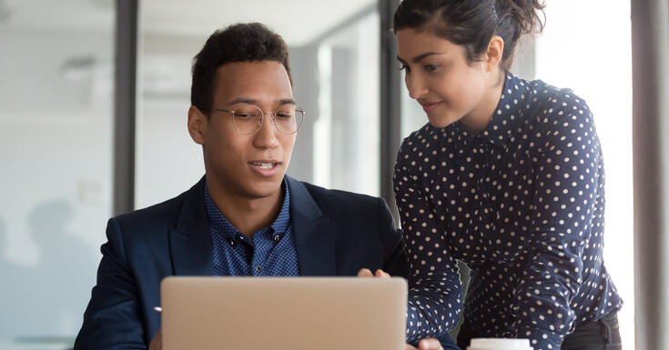 A tax technology professional assists another, using his laptop, in order to implement a seamless ERP upgrade.